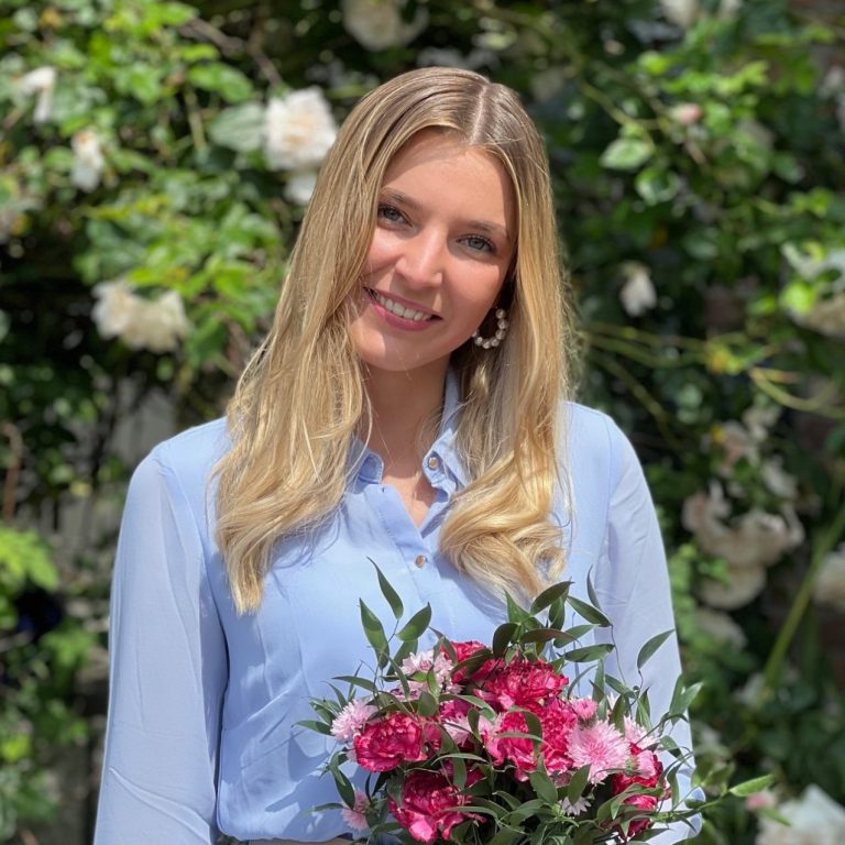 Louisa lächelt in die Kamera mit einem Strauß Blumen in der Hand
