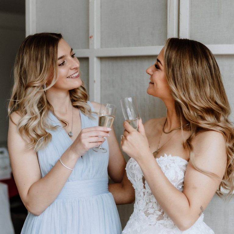 Amelie und Louisa stoßen mit einem Glas Sekt an und lächeln sich an